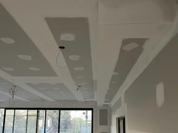 A coffered ceiling built from several bulkhead returns over a wall of glass sliding doors, set flush at every internal angle.