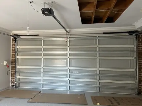 A garage ceiling pulled down to the joists with the old sheets stacked on the floor, ready for new board to be fixed up.